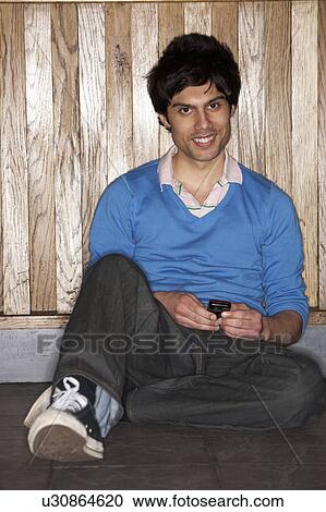 Stock Image - Young man sitting on floor with mobile phone. Fotosearch