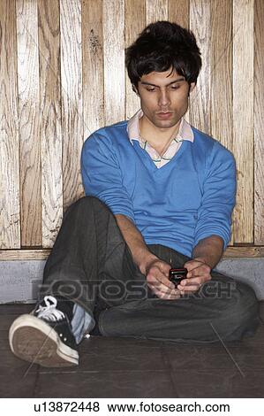 Stock Photo - Young man sitting on floor with mobile phone. Fotosearch