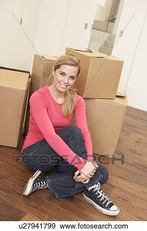 Stock Photo - Young woman on moving day sitting on floor among cardboard boxes. Fotosearch