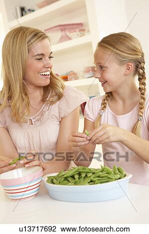 Stock Image - Young woman with child splitting pea in kitchen. Fotosearch