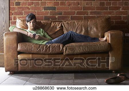 Stock Image - Young woman with phone on sofa. Fotosearch