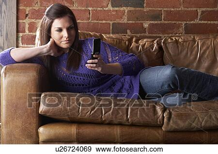 Stock Photo - Young woman with phone on sofa. Fotosearch