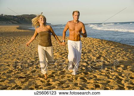 Stock Image - Couple running at beach. Fotosearch