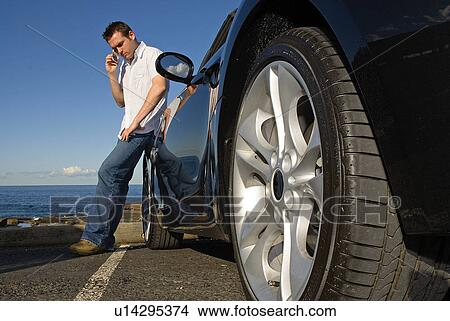 Picture - Man leaning against his car on the phone. Fotosearch