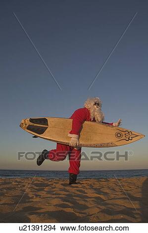 Picture - Santa carrying surfboard on beach. Fotosearch
