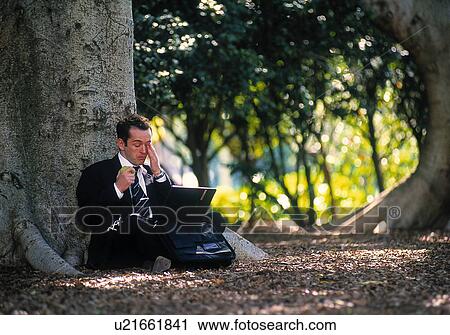 Stock Image - Stressed businessman working on a laptop in a park. Fotosearch