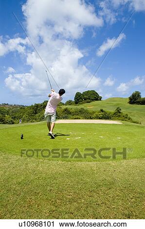 Stock Image - A late twenties male golfer tees off. Fotosearch
