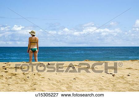 Stock Photo - A mid twenties white female in a green bathing suit standing at the beach in Kauai Hawaii. Fotosearch