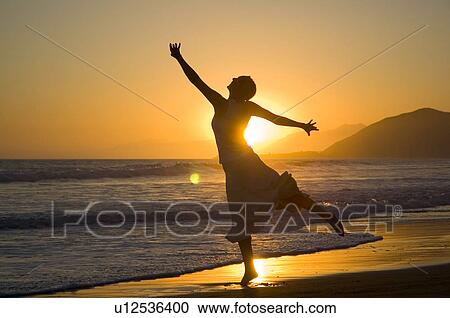 Stock Image - A young female on the beach at sunset. Fotosearch