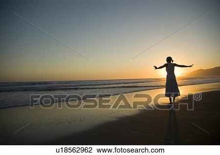 Stock Image - A young female on the beach at sunset. Fotosearch