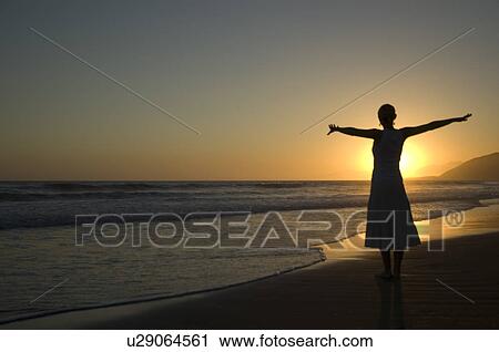 Stock Image - A young female on the beach at sunset. Fotosearch