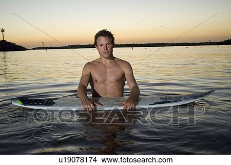 Picture - A young male surfer in the water after sunset. Fotosearch