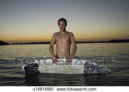 Stock Image - A young male surfer in the water after sunset. Fotosearch