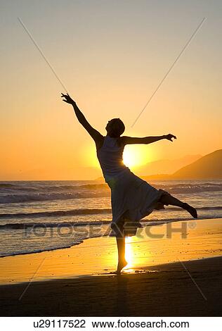 Stock Image - A young woman dances ballet on the beach at sunset. Fotosearch