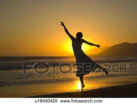 Stock Photography - A young woman dances ballet on the beach at sunset. Fotosearch