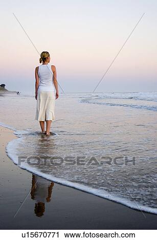Stock Image - A young woman walks on the beach at sunset. Fotosearch