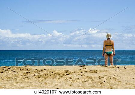 Stock Photo - Female in a green bathing suit standing on the beach in Kauai Hawaiian Islands USA. Fotosearch