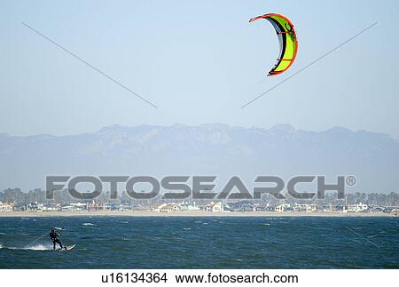Picture - Individual kiteboarding with beach community in the background. Fotosearch