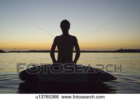 Stock Photograph - Male surfer in the water after sunset. Fotosearch