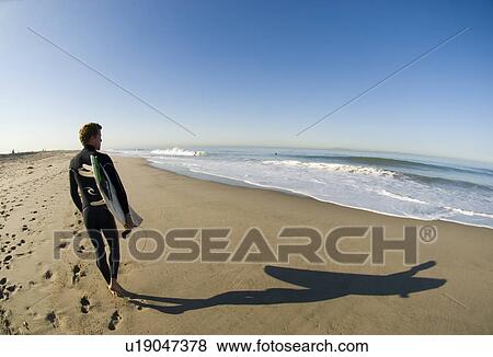 Stock Photo - Male surfer waking down the beach. Fotosearch