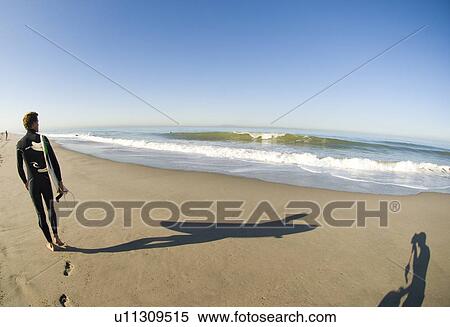 Stock Photography - Male surfer waking down the beach. Fotosearch