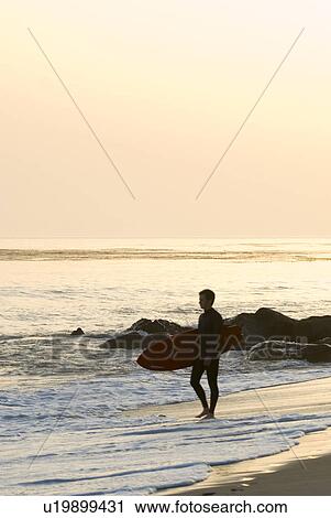 Stock Image - Male with a surfboard at sunset. Fotosearch