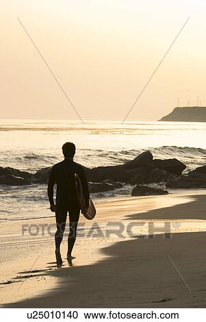 Stock Image - Male with a surfboard at sunset. Fotosearch