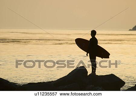 Stock Photo - Male with a surfboard at sunset. Fotosearch
