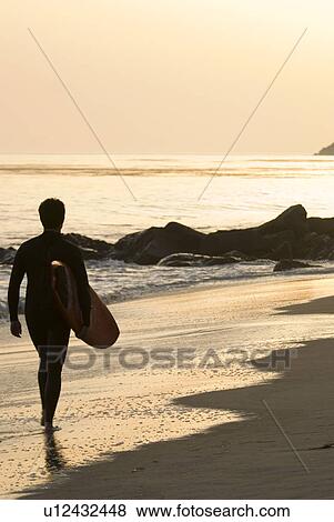 Stock Photo - Male with a surfboard at sunset. Fotosearch
