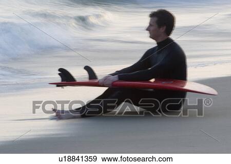Man holding a surfboard sitting on the beach View Large Photo Image Stock Photo - Man holding a surfboard sitting on the beach. Fotosearch