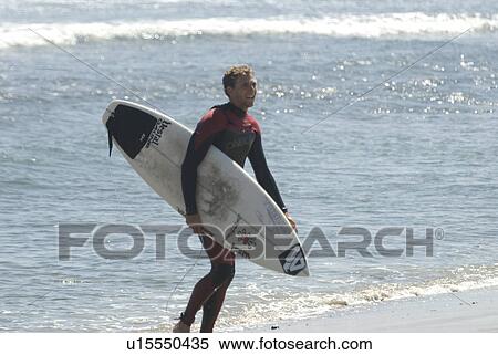 Stock Photography - Man in wetsuit carrying surfboard. Fotosearch