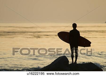 Stock Photography - Surfer on a rock at sunset. Fotosearch