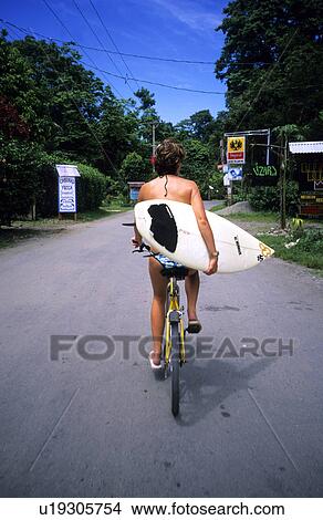 Woman riding bike carrying surfboard View Large Photo Image Picture - Woman riding bike carrying surfboard. Fotosearch