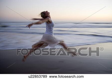 Stock Photo - Young female on the beach jumping at sunset. Fotosearch