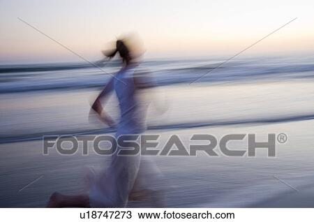 Stock Image - Young female running on the beach at sunset. Fotosearch