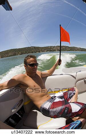 Stock Image - Young male raising a flag on a boat. Fotosearch