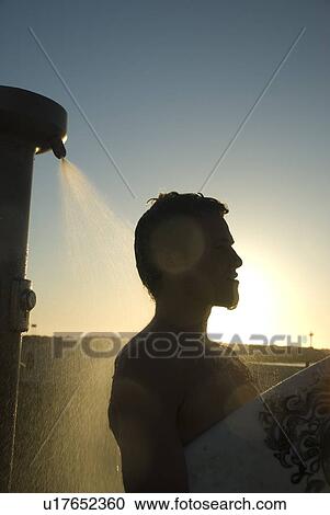 Stock Image - Young male surfer rinsing off in the shower. Fotosearch