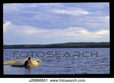 Stock Image - Boy sitting on a rock in the water. Fotosearch