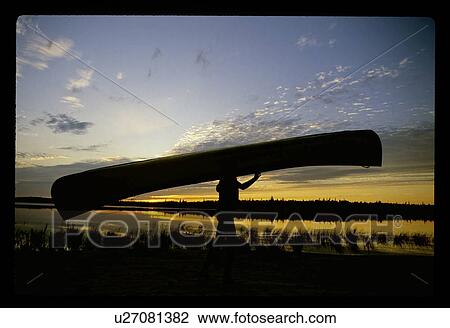 Stock Image - Carrying a canoe at sunset. Fotosearch
