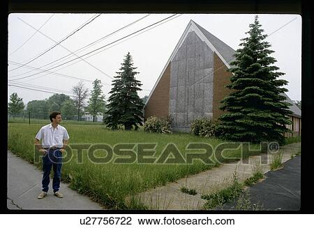 Stock Image - Man standing by a boarded up church. Fotosearch