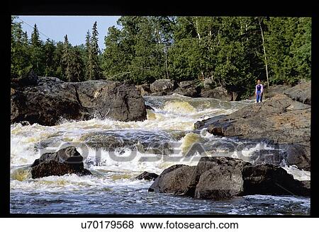 Stock Photo - Person standing on rock overlooking river. Fotosearch
