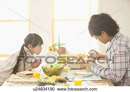 Stock Image - Daughter Watching Father at Breakfast Table. Fotosearch