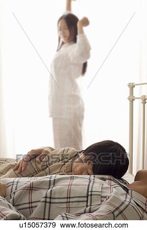 Stock Photo - Father and Daughter Sleeping, Mother Stretching in Background. Fotosearch