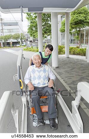 Stock Image - Healthcare worker helping senior man in wheelchair getting into a van, Kanagawa Prefecture, Honshu, Japan. Fotosearch