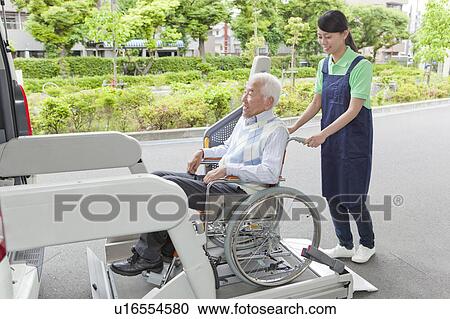 Stock Image - Healthcare worker helping senior man in wheelchair getting into a van, Kanagawa Prefecture, Honshu, Japan. Fotosearch