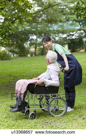 Stock Photo - Healthcare worker pushing senior man in wheelchair, Tokyo Prefecture, Honshu, Japan. Fotosearch