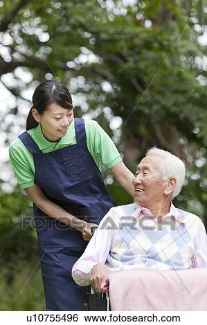 Stock Photograph - Healthcare worker pushing senior man in wheelchair, Tokyo Prefecture, Honshu, Japan. Fotosearch