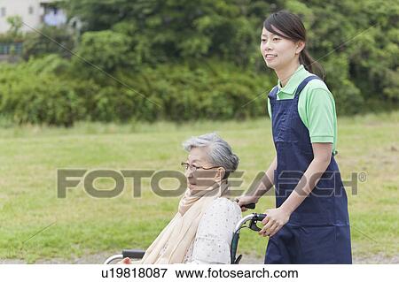 Stock Photo - Healthcare worker pushing senior woman in wheelchair, Tokyo Prefecture, Honshu, Japan. Fotosearch