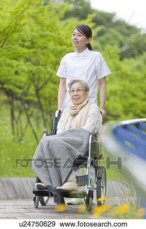 Stock Photo - Healthcare worker pushing senior woman in wheelchair, Kanagawa Prefecture, Honshu, Japan. Fotosearch