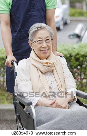 Stock Photo - Healthcare worker pushing senior woman in wheelchair, Kanagawa Prefecture, Honshu, Japan. Fotosearch